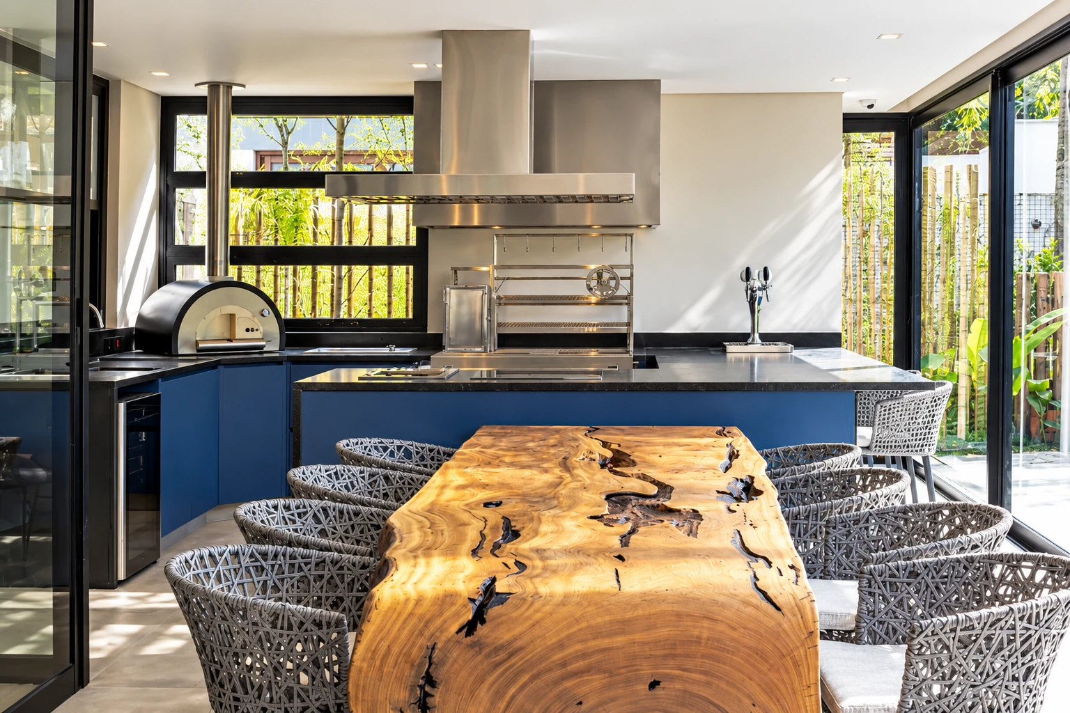 Área gourmet com ilha azul, forno de pizza e churrasqueira em inox